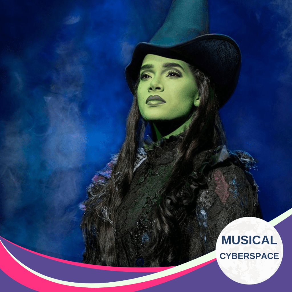 Lencia Kebede as Elphaba in WICKED, standing in a cloud of smoke with iconic green makeup and witch’s hat, with Musical Cyberspace branding overlay.