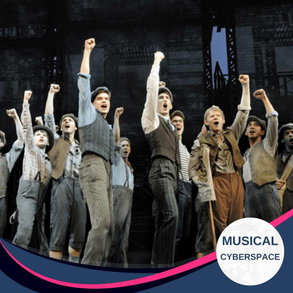 A large group of newsboys in flat caps and suspenders thrust their fists into the air in unison, shouting in solidarity against an industrial backdrop, in a scene from Newsies’ “Seize the Day.”