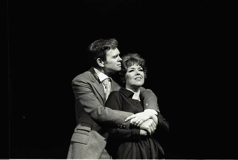 Black-and-white production photograph from The Fig Leaves Are Falling showing Barry Nelson standing behind Dorothy Loudon, holding her as she looks outward with a wry expression. Both are in 1960s-style costumes against a plain dark stage background.
